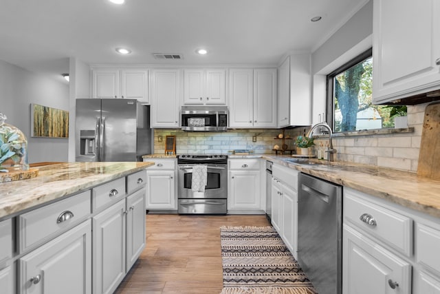 kitchen featuring light stone counters, white cabinets, sink, backsplash, and appliances with stainless steel finishes