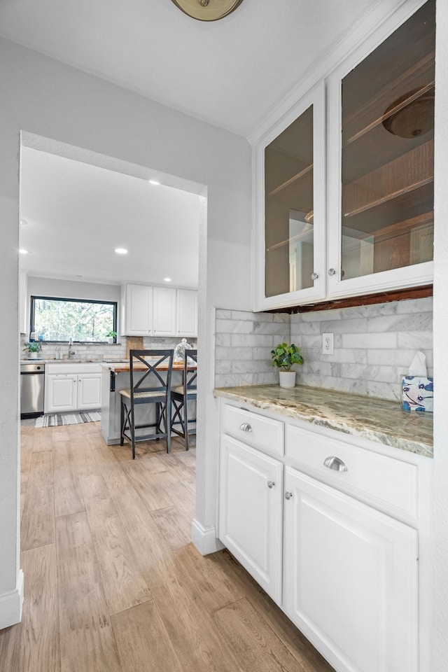 kitchen featuring light stone counters, stainless steel dishwasher, backsplash, white cabinetry, and light wood-type flooring