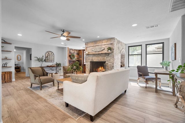 living room with a stone fireplace, light wood-type flooring, and ceiling fan