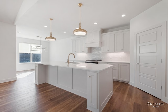 kitchen with white cabinetry, stainless steel range, sink, hanging light fixtures, and an island with sink