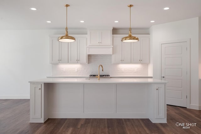 kitchen featuring hanging light fixtures, white cabinets, an island with sink, and dark hardwood / wood-style floors