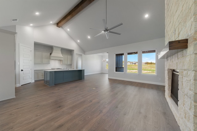 unfurnished living room featuring ceiling fan, beam ceiling, hardwood / wood-style flooring, high vaulted ceiling, and a stone fireplace