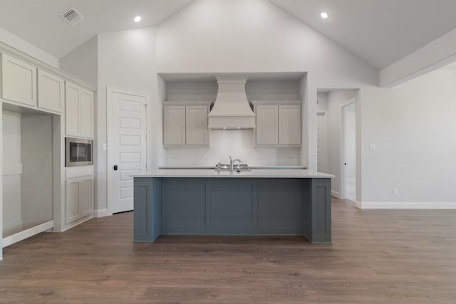 kitchen with dark hardwood / wood-style flooring, premium range hood, high vaulted ceiling, stainless steel microwave, and an island with sink