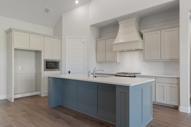 kitchen with black microwave, an island with sink, dark hardwood / wood-style floors, and custom range hood