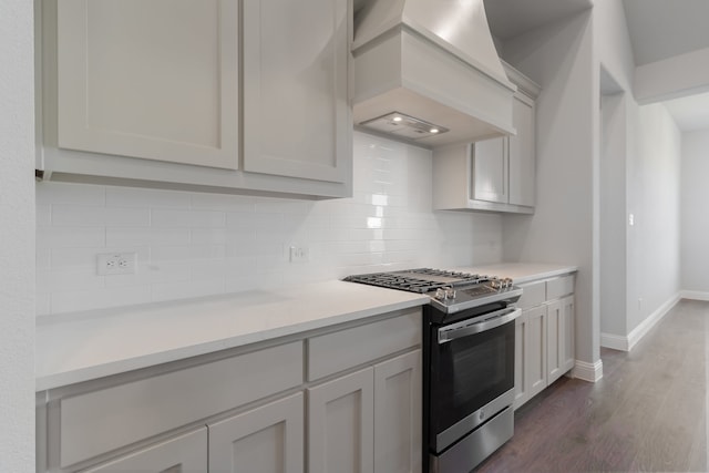 kitchen featuring gas range, dark hardwood / wood-style floors, decorative backsplash, white cabinets, and custom range hood