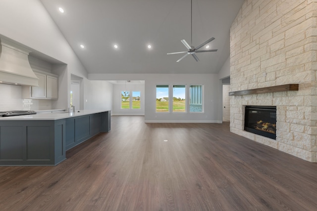 unfurnished living room with dark hardwood / wood-style flooring, a stone fireplace, ceiling fan with notable chandelier, and high vaulted ceiling