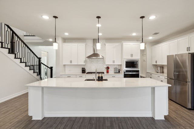 kitchen featuring stainless steel appliances, a large island, wall chimney range hood, and white cabinets