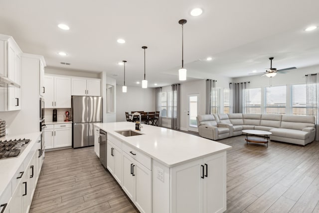 kitchen featuring sink, white cabinetry, stainless steel appliances, a center island with sink, and decorative light fixtures