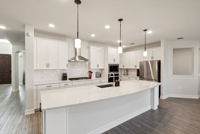 kitchen featuring sink, hanging light fixtures, an island with sink, white cabinets, and wall chimney exhaust hood