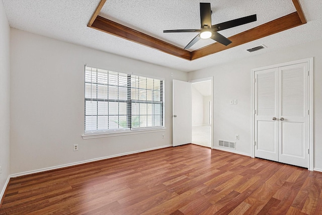 unfurnished bedroom featuring a tray ceiling, visible vents, and wood finished floors