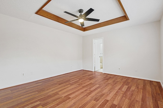 unfurnished room featuring a raised ceiling, light wood finished floors, and ceiling fan