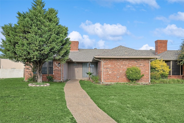 ranch-style home featuring a shingled roof, a front lawn, brick siding, and a chimney