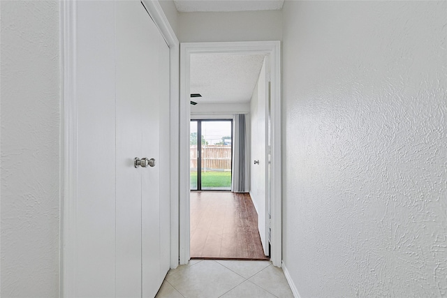 hall featuring light tile patterned flooring, a textured wall, baseboards, and a textured ceiling