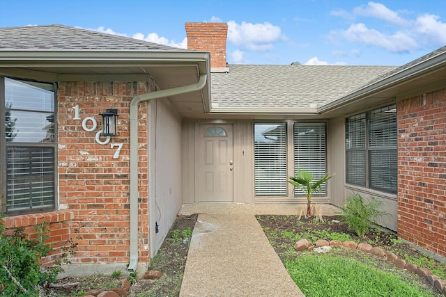 entrance to property featuring brick siding, a chimney, and a shingled roof