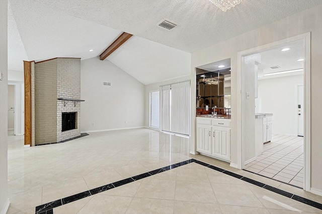 unfurnished living room with visible vents, baseboards, lofted ceiling with beams, a sink, and a textured ceiling