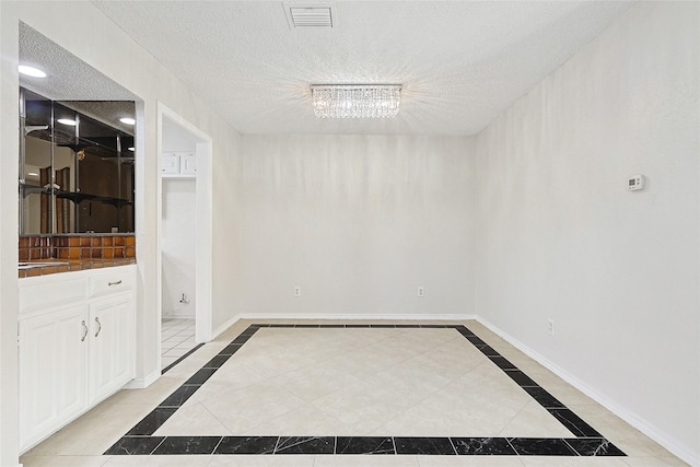 spare room featuring tile patterned flooring, visible vents, a textured ceiling, and baseboards