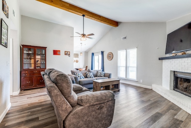 living room featuring a brick fireplace, wood-type flooring, beamed ceiling, and ceiling fan