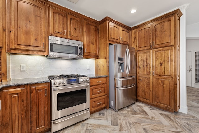 kitchen with light parquet flooring, appliances with stainless steel finishes, dark stone counters, and backsplash