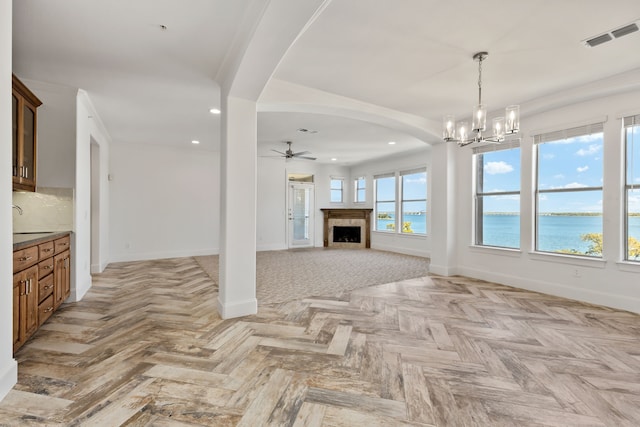 unfurnished living room featuring a water view, baseboards, arched walkways, recessed lighting, and ceiling fan with notable chandelier
