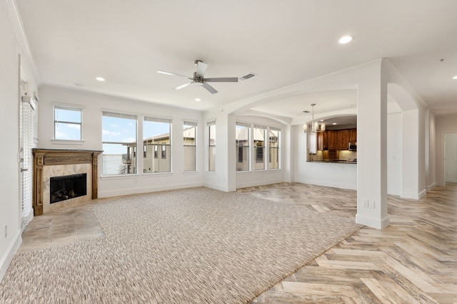 unfurnished living room featuring light parquet floors, a high end fireplace, ornamental molding, and ceiling fan with notable chandelier