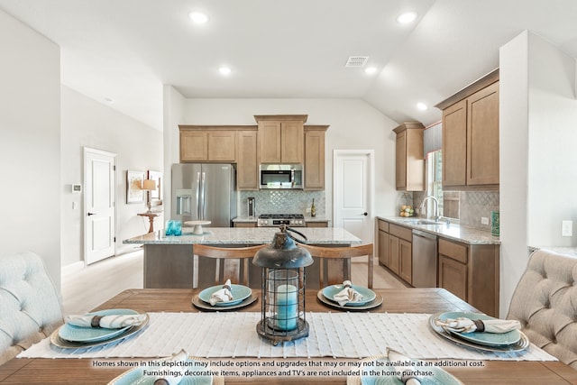 kitchen with appliances with stainless steel finishes, a breakfast bar area, backsplash, a center island, and vaulted ceiling