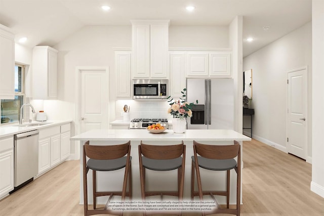 kitchen featuring white cabinets, a sink, stainless steel appliances, backsplash, and a kitchen island