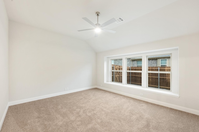 empty room with baseboards, vaulted ceiling, carpet floors, visible vents, and ceiling fan