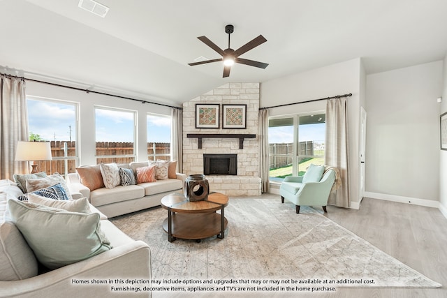 living room featuring ceiling fan, a stone fireplace, light wood-type flooring, and vaulted ceiling