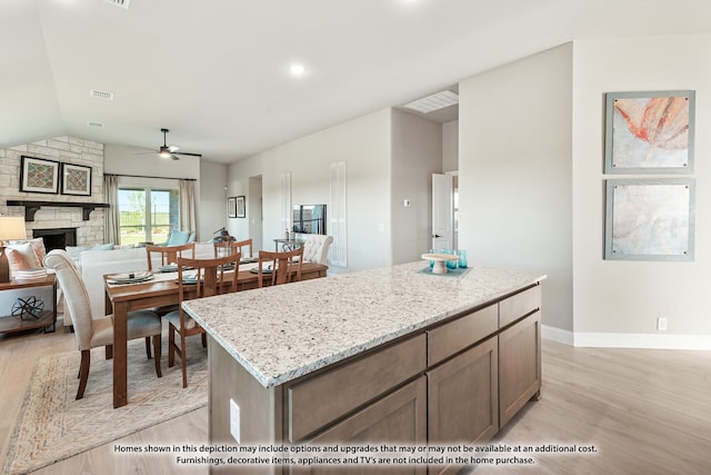 kitchen with light stone counters, ceiling fan, a fireplace, light hardwood / wood-style flooring, and a kitchen island