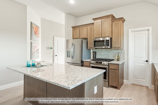 kitchen featuring stainless steel appliances, a center island, light stone counters, decorative backsplash, and light wood-type flooring