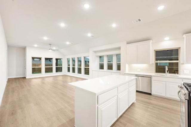 kitchen with appliances with stainless steel finishes, a kitchen island, visible vents, ceiling fan, and a sink