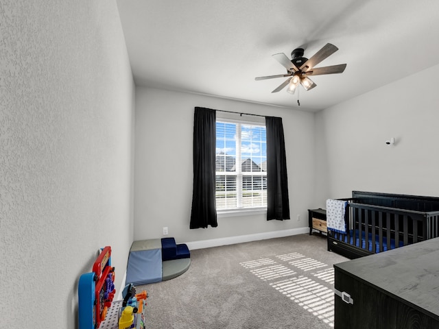 carpeted bedroom with ceiling fan and a crib