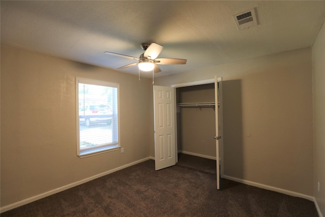 unfurnished bedroom featuring dark colored carpet, ceiling fan, a textured ceiling, and a closet