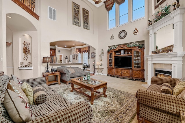 living room featuring a towering ceiling, a tile fireplace, and crown molding