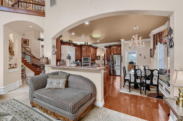 kitchen with ornamental molding, stainless steel appliances, light stone countertops, light hardwood / wood-style floors, and kitchen peninsula