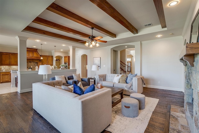 living room featuring crown molding, a stone fireplace, beam ceiling, dark wood-type flooring, and ceiling fan