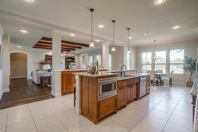 kitchen featuring sink, light tile patterned floors, a kitchen island with sink, appliances with stainless steel finishes, and decorative light fixtures