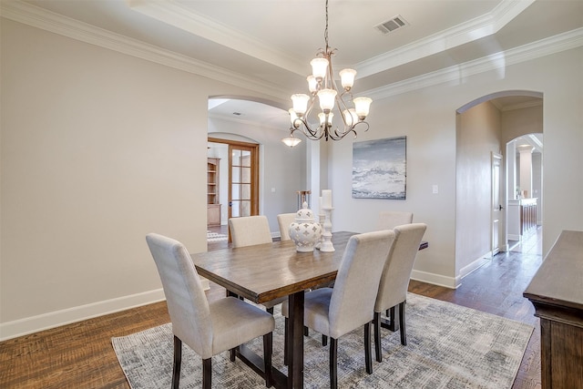 dining area with a raised ceiling, dark wood-type flooring, a chandelier, and crown molding