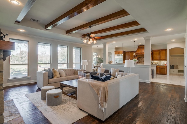 living room featuring ceiling fan with notable chandelier, dark wood-type flooring, and beamed ceiling