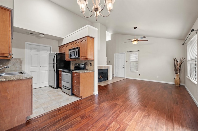 kitchen featuring sink, stainless steel appliances, light hardwood / wood-style floors, a tiled fireplace, and decorative backsplash