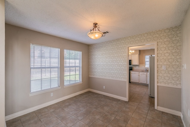 empty room with a chandelier, a textured ceiling, and tile patterned floors