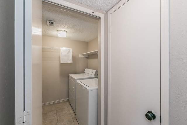 laundry room featuring washing machine and clothes dryer, light tile patterned flooring, and a textured ceiling