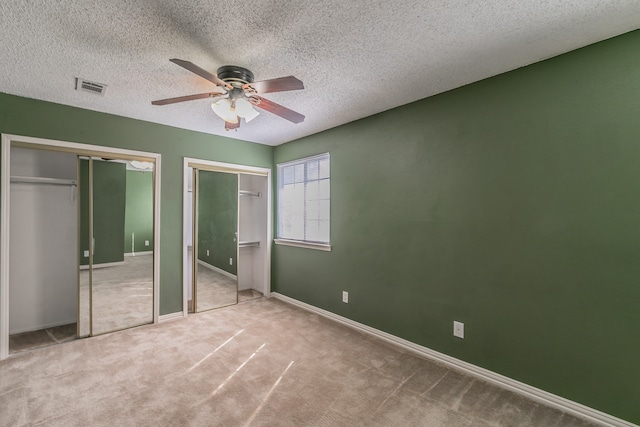 unfurnished bedroom with a textured ceiling, two closets, ceiling fan, and carpet floors