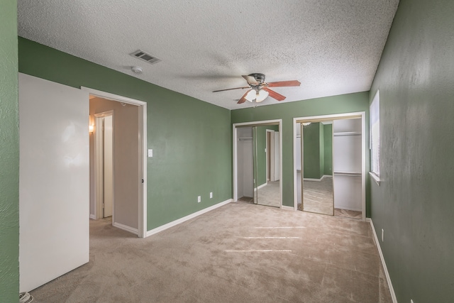 unfurnished bedroom featuring ceiling fan, a textured ceiling, light carpet, and two closets