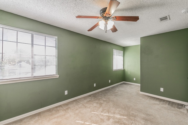 carpeted spare room with a wealth of natural light, a textured ceiling, and ceiling fan