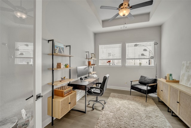 office featuring light hardwood / wood-style floors, ceiling fan, and a tray ceiling