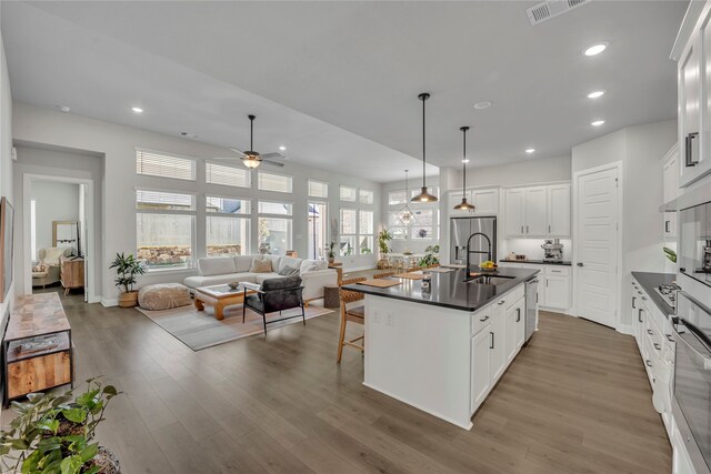 kitchen featuring white cabinetry, hardwood / wood-style flooring, pendant lighting, and an island with sink