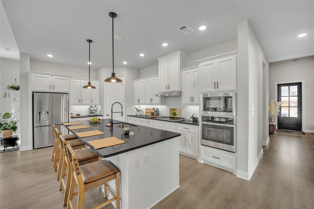 kitchen with sink, appliances with stainless steel finishes, hanging light fixtures, light hardwood / wood-style flooring, and white cabinets