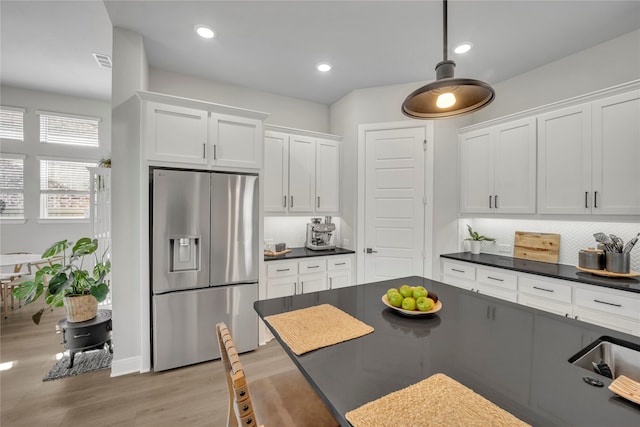 kitchen with tasteful backsplash, light wood-type flooring, stainless steel refrigerator with ice dispenser, and white cabinets