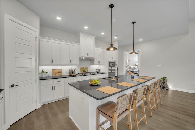 kitchen with light hardwood / wood-style floors, white cabinetry, a kitchen bar, hanging light fixtures, and a kitchen island with sink